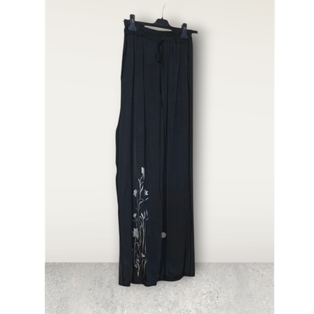 Pantalón negro satinado con dibujo de flor blanca — colección Cruella | Artesania Textil
